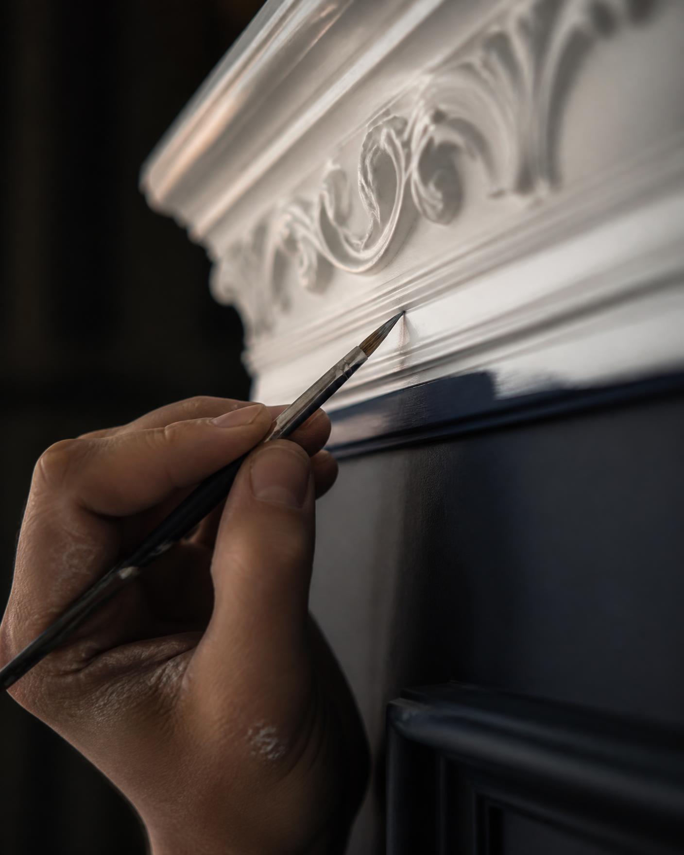 Decorator cutting in a fine paint line against ornate white cornice detail